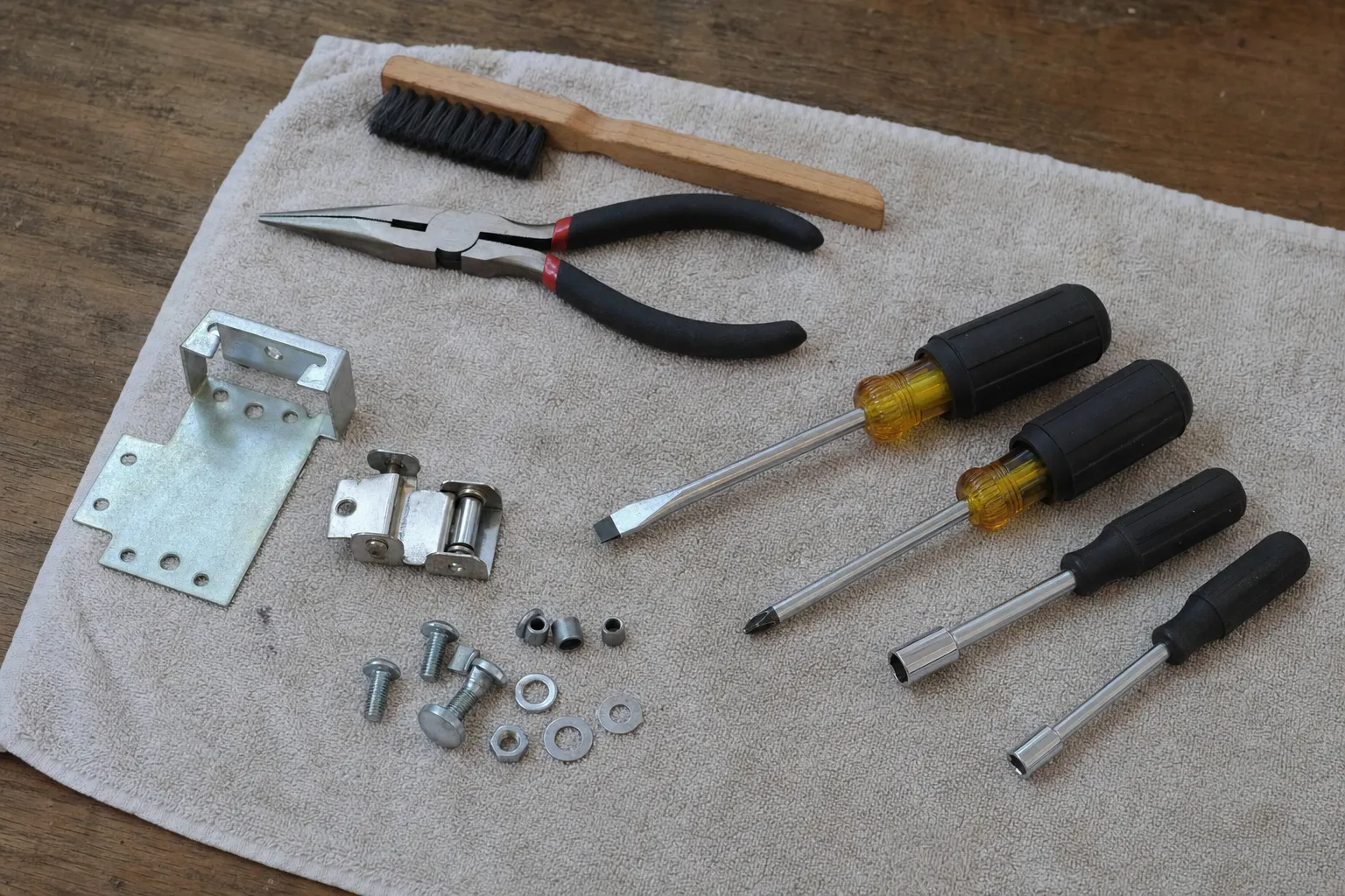 Folded towel holding a dismantled door hinge, mounting brackets, screwdrivers, pliers and fixings